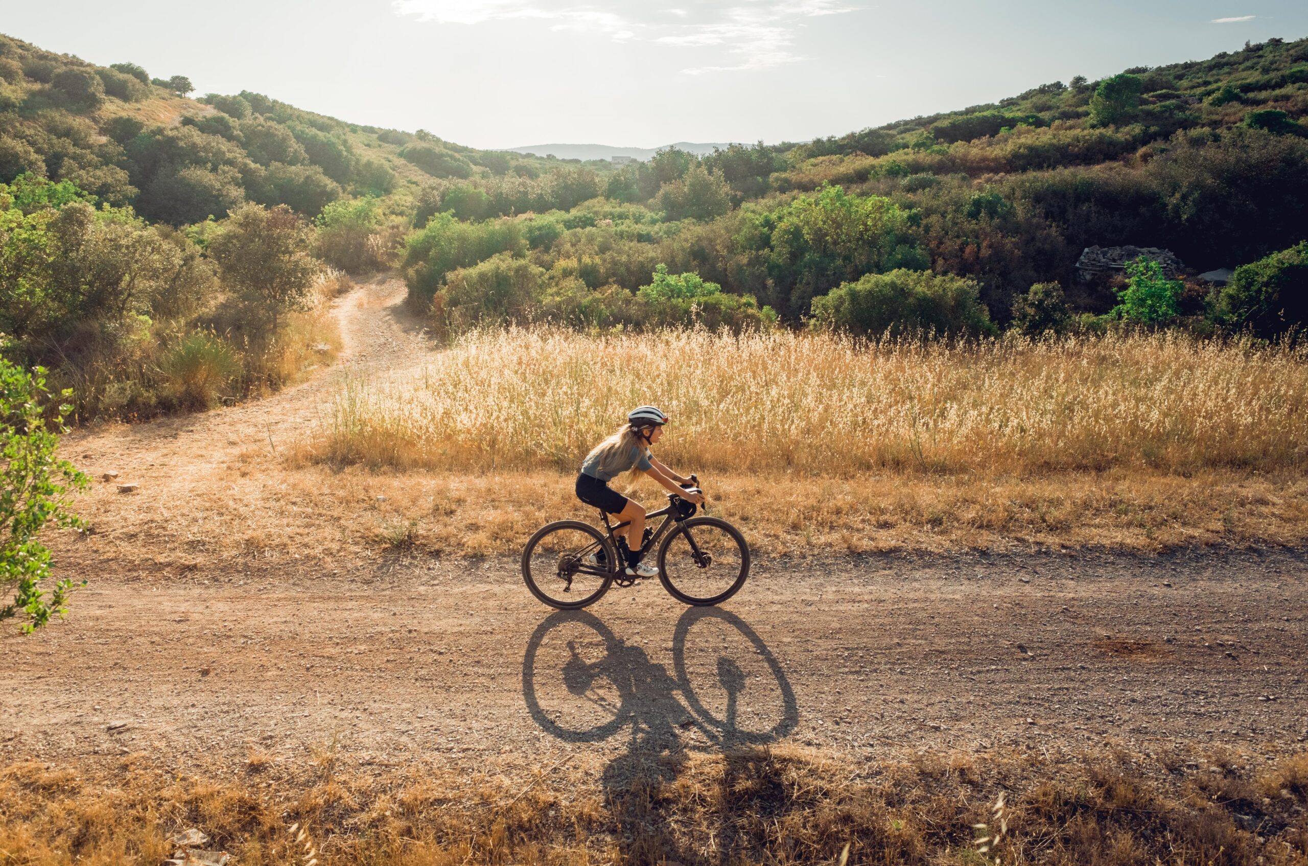 Cyclist riding gravel from side in golden fields